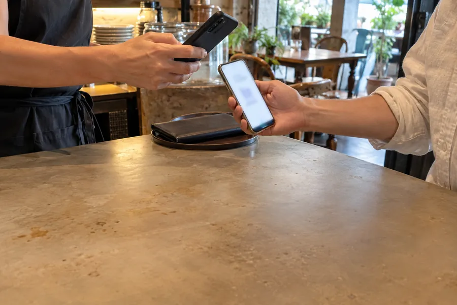 An der Theke eines Restaurants scannt jemand vom Personal mit dem Handy das Handy, das ein Gast hinhält
